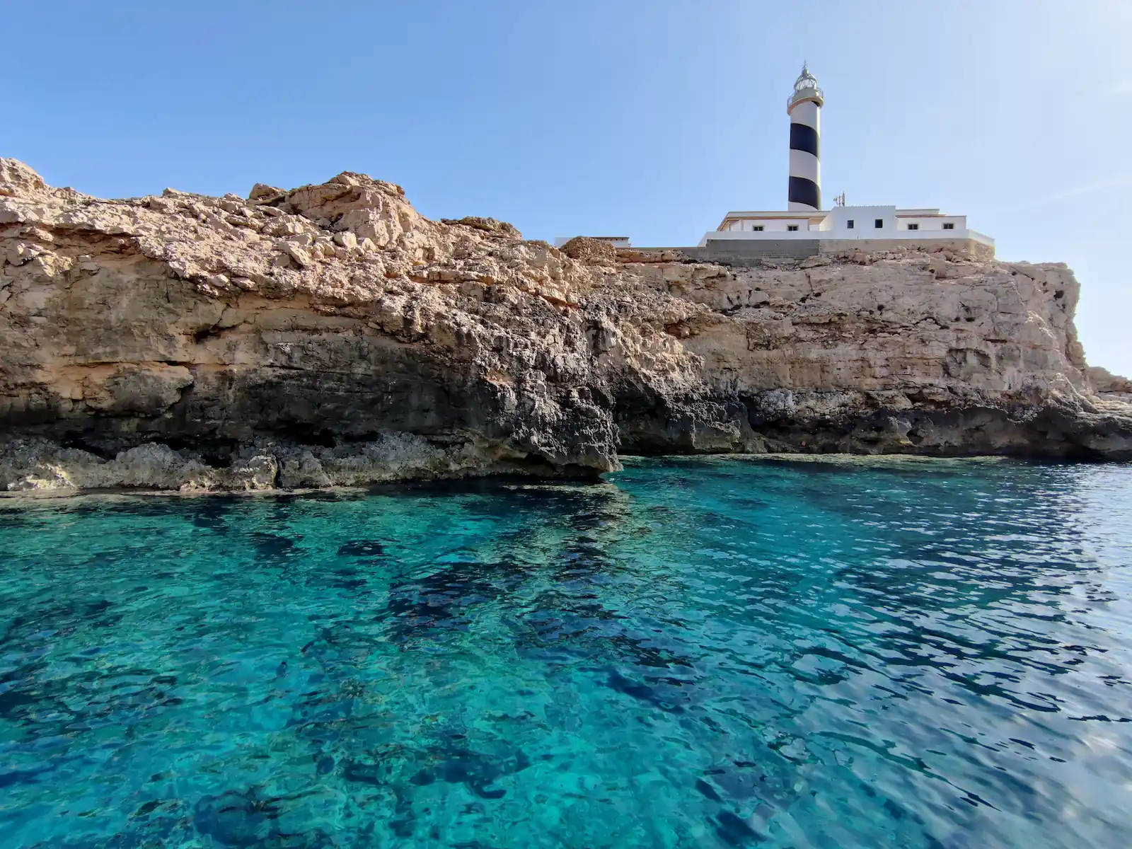 Leuchtturm auf Felsenküste mit türkisem Wasser im Vordergrund